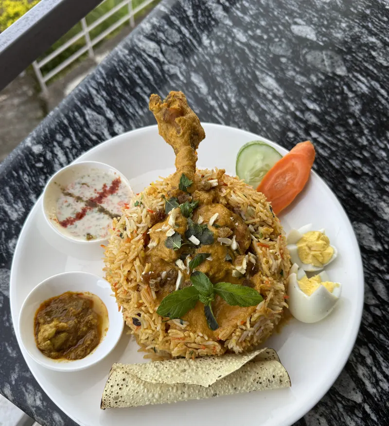 Chicken biryani with raita, curry, egg and papad on a terrace table