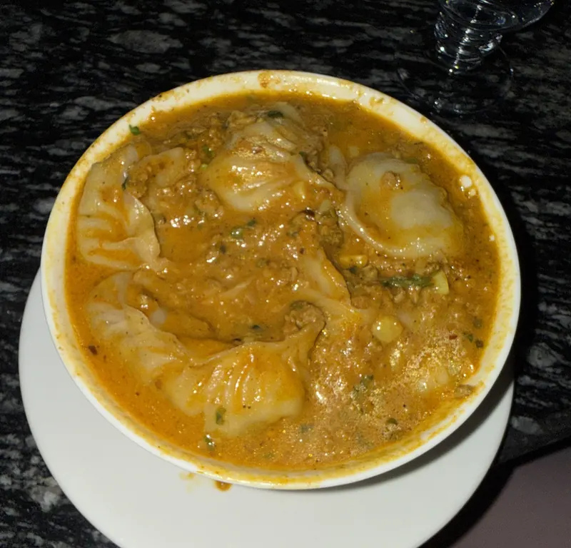 A bowl of jhol momo in sesame-tomato sauce, seen from above