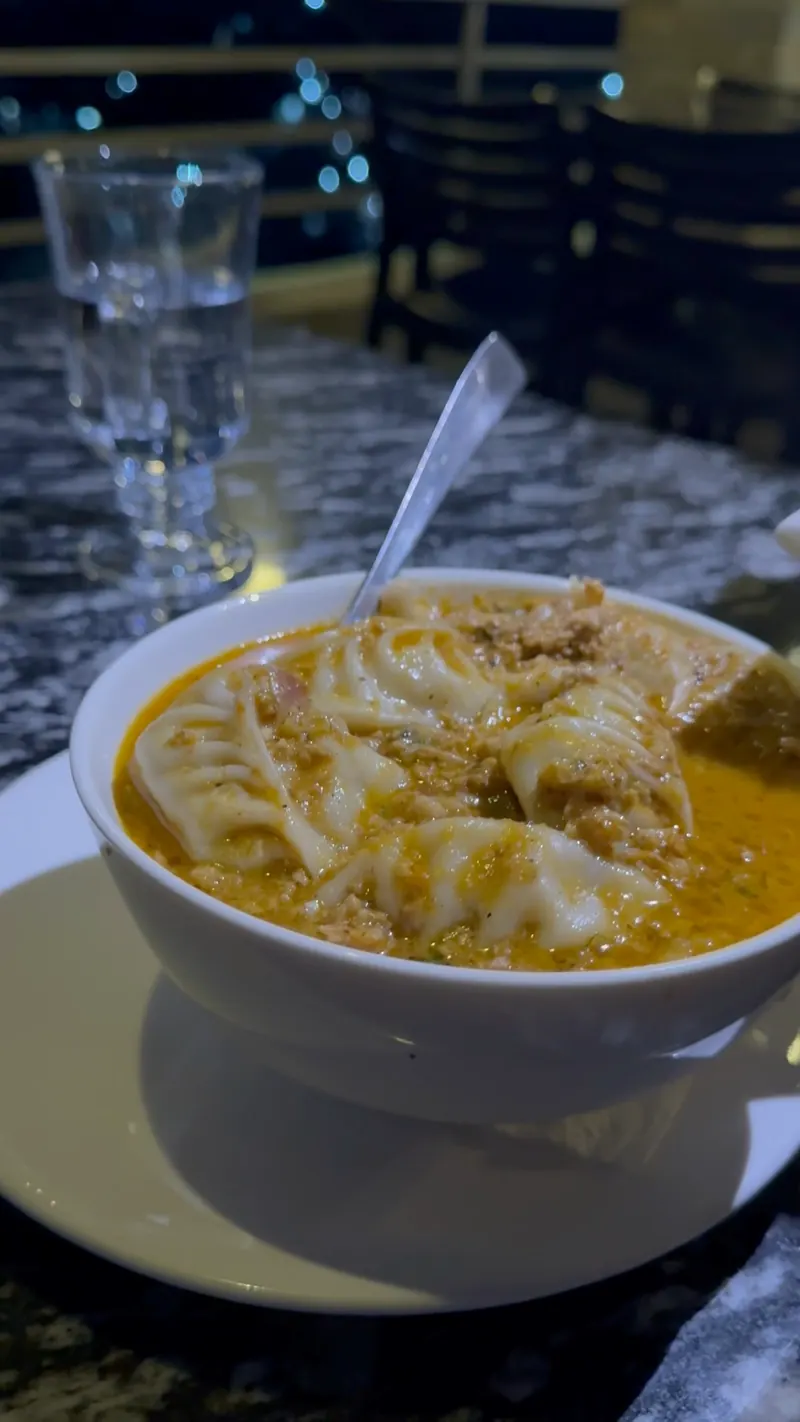 A bowl of jhol momo on the terrace at night with city lights in the distance