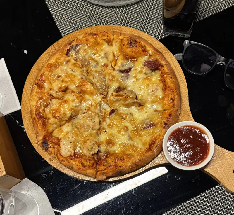Meat Lovers pizza on a wooden board with a bowl of sauce