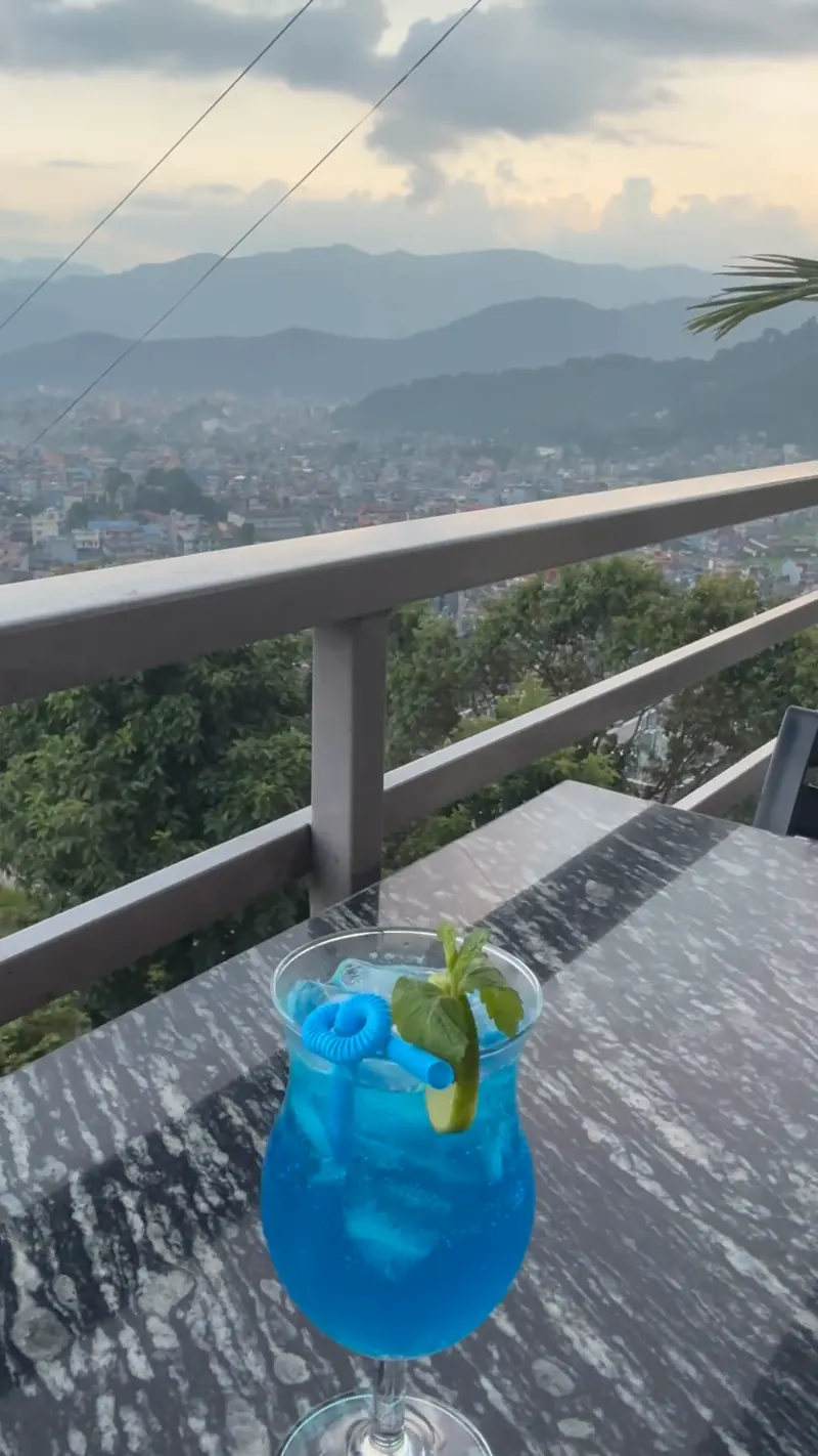 A blue drink on the terrace railing at sunset, hills and Pokhara behind